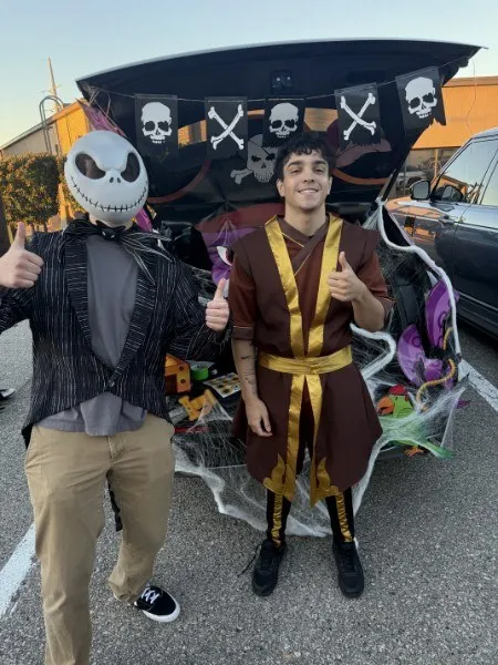 Two adults in costume beside a decorated trunk at a past Trunk or Treat